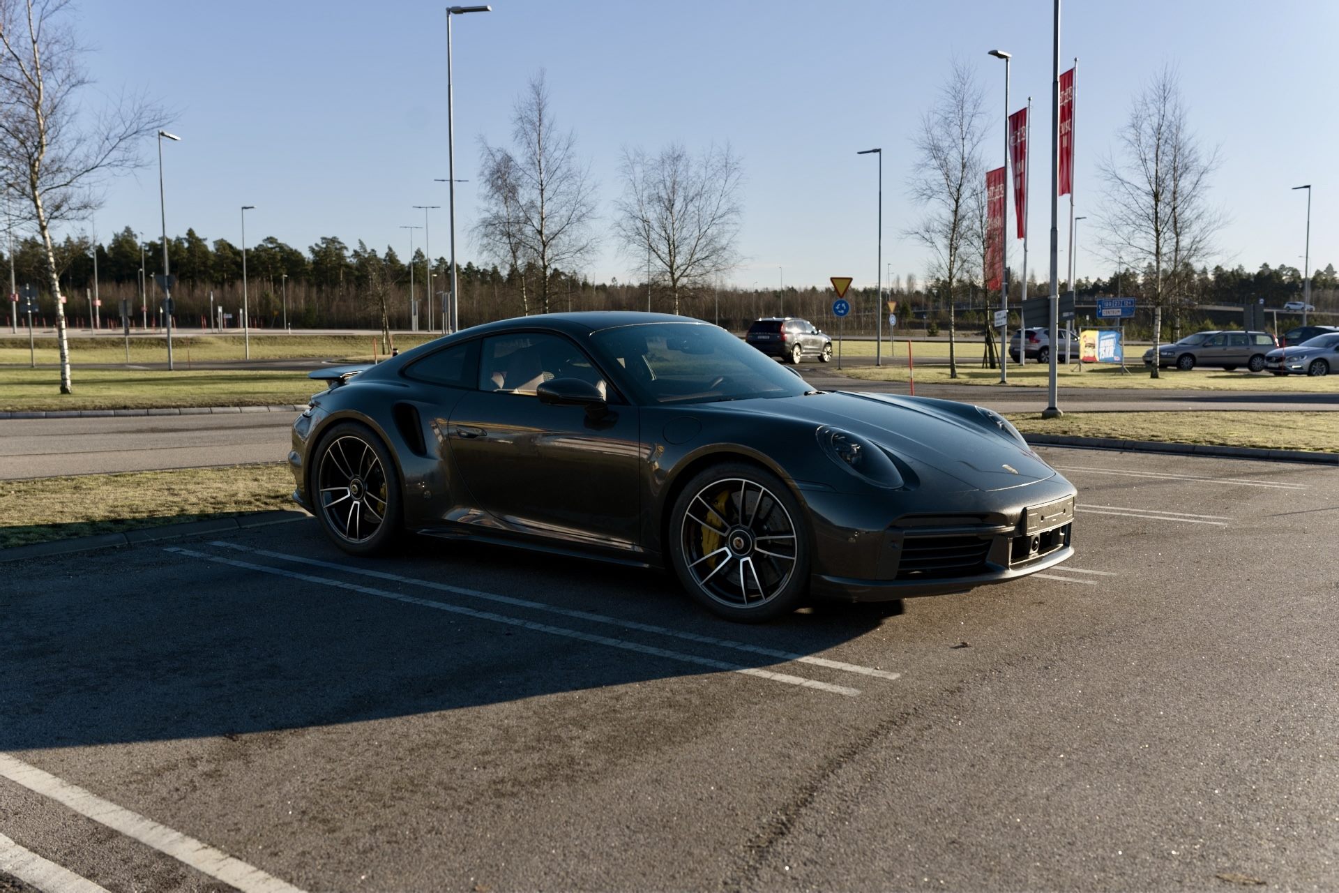 Dark grey Porsche 911 parked in a car park with bare trees behind it