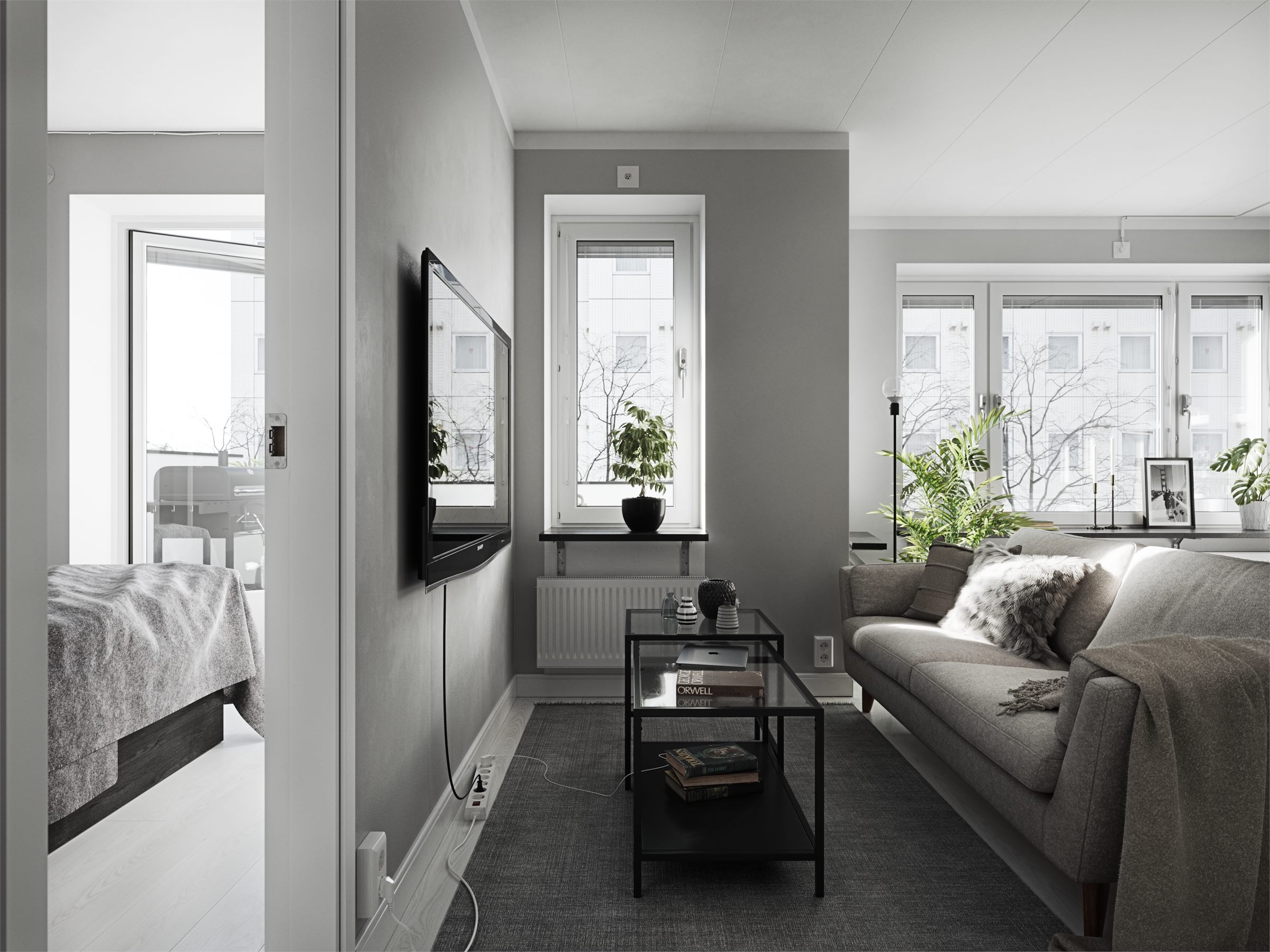 Living room with a beige sofa, a dark coffee table, plants and a view into a bedroom