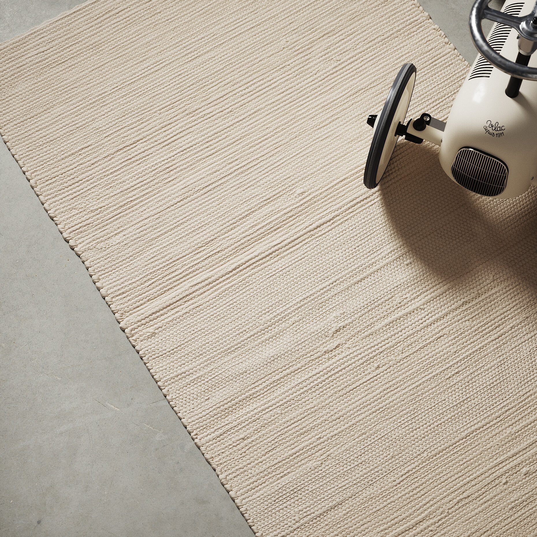 Woven straw-coloured rug on a concrete floor with a small white toy