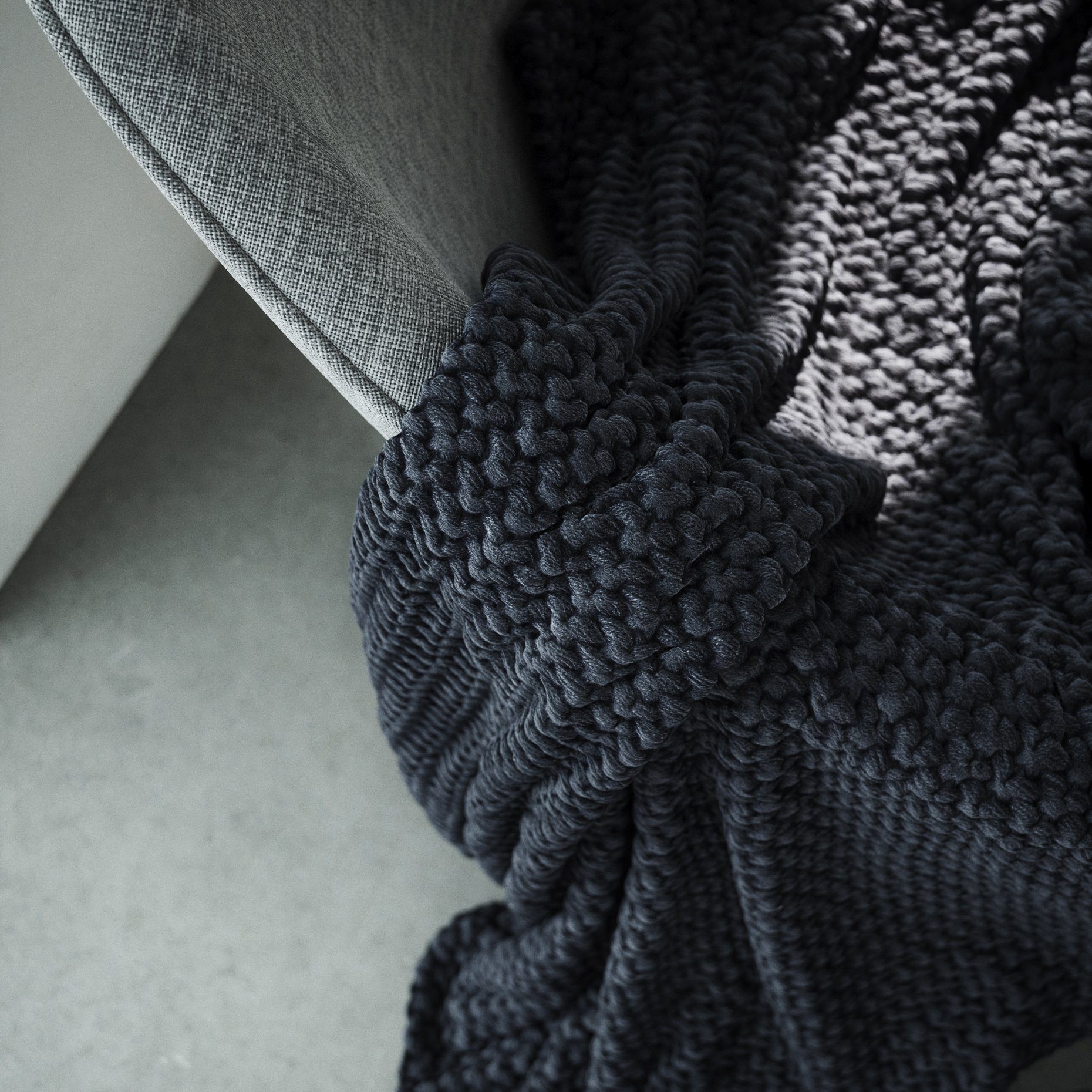 Close-up of a dark knitted throw resting on a grey surface